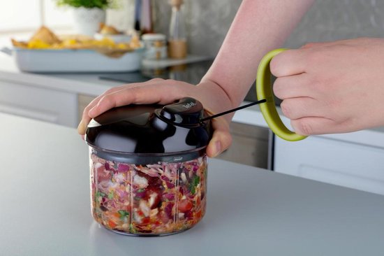 Een hand die de lus van een Tefal hakmolen trekt, met fijngesneden groenten in de container.