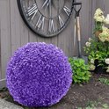 Paarse sierbal van kunstplantjes, in een tuin naast planten en een grote klok.