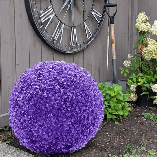 Paarse sierbal van kunstplantjes, in een tuin naast planten en een grote klok.