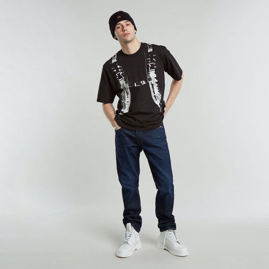 Man in donkerblauwe G-Star Mosa jeans, zwart T-shirt met print en zwarte muts.