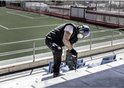 Man met een blauwe helm en gehoorbescherming gebruikt een Bosch boorhamer bij een stadion.