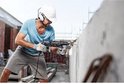 Man met helm boort in een betonnen muur met een Bosch boor.