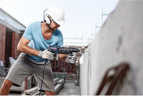 Man met helm boort in een betonnen muur met een Bosch boor.