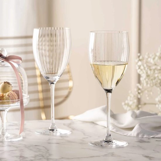 Twee glazen met verticale ribbels op een marmeren ondergrond. Eén glas is gevuld met witte wijn.