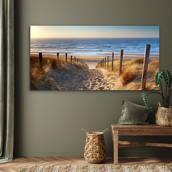 Un sentier à travers les dunes, bordé d'herbes, mène à la mer au coucher du soleil.