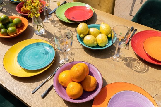 Een tafel gedekt met kleurrijke borden, kommen met sinaasappels, citroenen en limoenen.