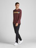 Man in een zwart broek met Jack & Jones logo shirt, staand.
