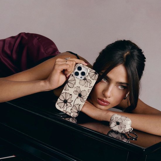Model met telefoonhoes met beige achtergrond en bloemenprint, naast airpod case.
