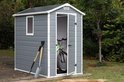 Grijs Manor Pent 6x4 tuinhuis met schuin dak, open deuren met fiets erin, op een houten dek.