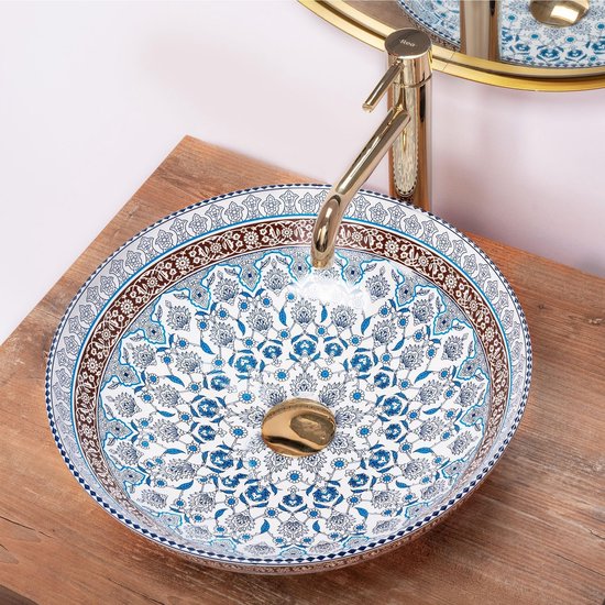Ronde wastafel met een Delfts blauw patroon, gouden kraan op een houten aanrechtblad, met spiegel.