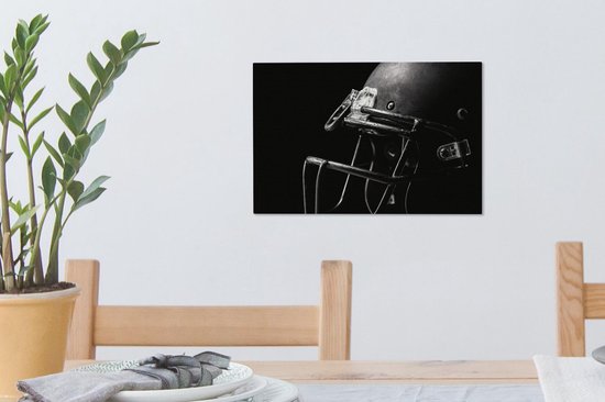 Un casque de football américain noir avec masque en acier, sur un mur à côté d'une plante.