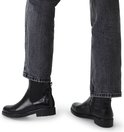 Model draagt zwarte leren chelsea boots met crocoprint en jeans.