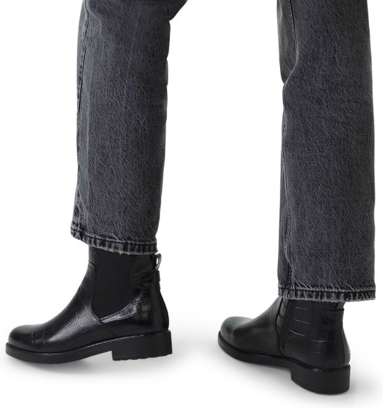 Model draagt zwarte leren chelsea boots met crocoprint en jeans.