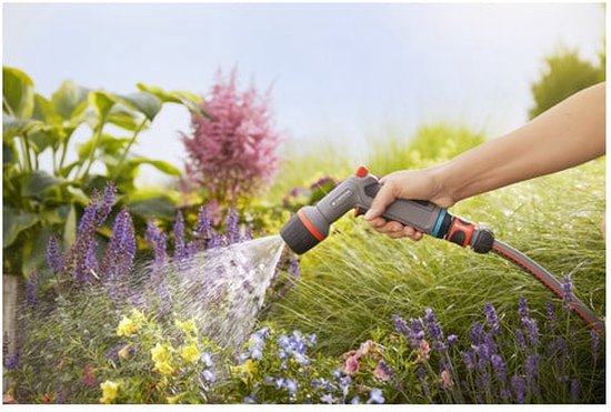 Hand sproeit bloemen in een tuin met een Gardena spuitpistool.