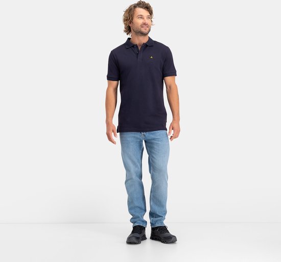 Man met kort blond haar, kijkend naar rechts, draagt een donkerblauw NOMAD poloshirt en spijkerbroek.
