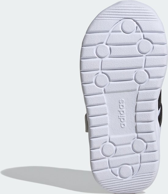 Onderkant van witte kindersneaker met zwart Adidas-logo en groeven.