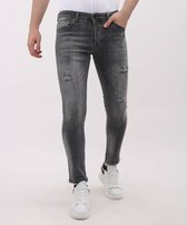 Model met grijze slim fit jeans, stonewashed met ripped details en witte spetters, en witte sneakers.
