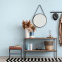Bruine kunstlederen hocker naast een console-tafel met decoratie en een spiegel aan een lichtblauwe muur.