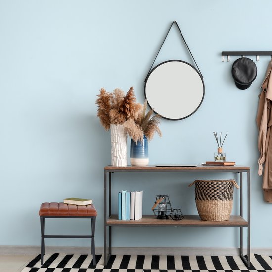 Bruine kunstlederen hocker naast een console-tafel met decoratie en een spiegel aan een lichtblauwe muur.