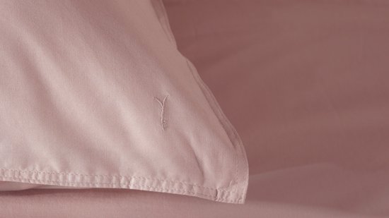 Close-up van een roze dekbedovertrek met een subtiel geborduurd logo.