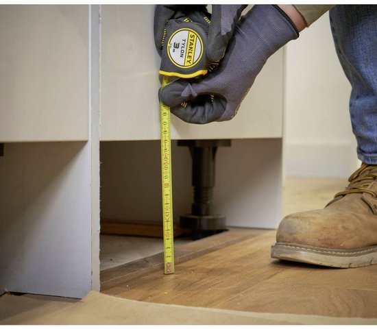 Man met grijze handschoenen meet de hoogte van keukenkastjes met een Stanley rolbandmaat.