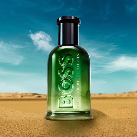 BOSS BOTTLED BOLD CITRUS Eau de Parfum fles in een zanderige woestijn onder een blauwe hemel.