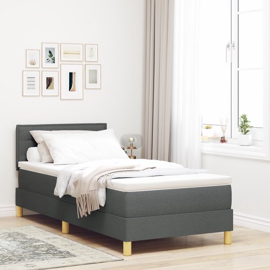 Donkergrijze boxspring opgemaakt met wit beddengoed en plaid, staand in een slaapkamer.