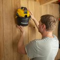 Een persoon hangt een gele en zwarte Powerplus nat-droog stofzuiger aan een houten muur.