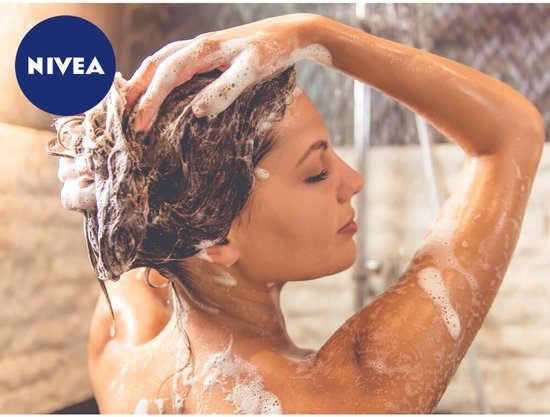 Femme aux yeux fermés se lave les cheveux sous la douche, avec beaucoup de mousse.