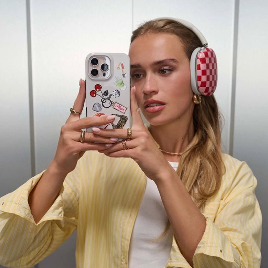 Vrouw met witte koptelefoon met rood-witte ruitjes, houdt een iPhone 15 met "It Girl" hoesje omhoog.