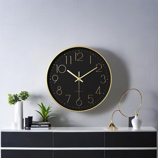 Zwarte wandklok met gouden rand en cijfers, hangend boven een dressoir in een hal.
