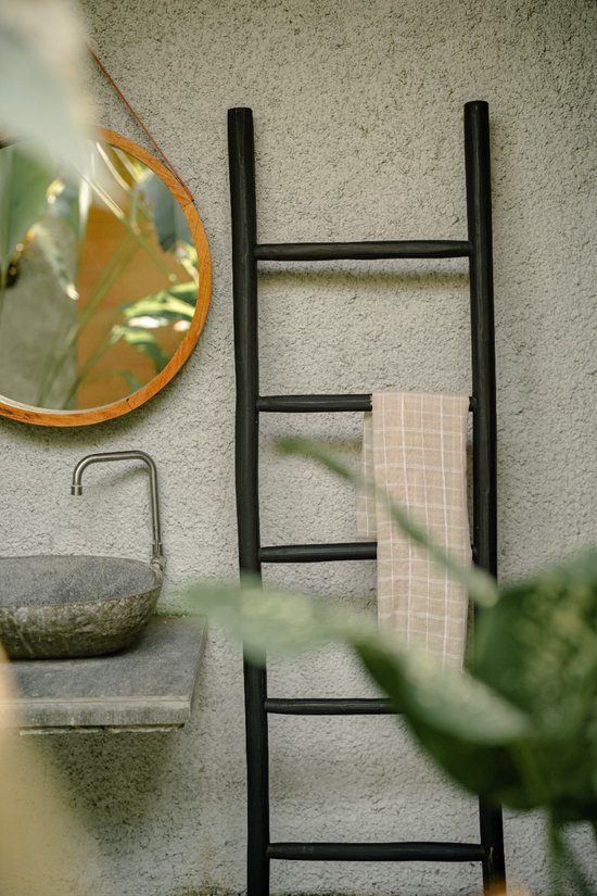 Zwarte houten decoratieve ladder met een beige geruite handdoek erop, in een badkameromgeving.