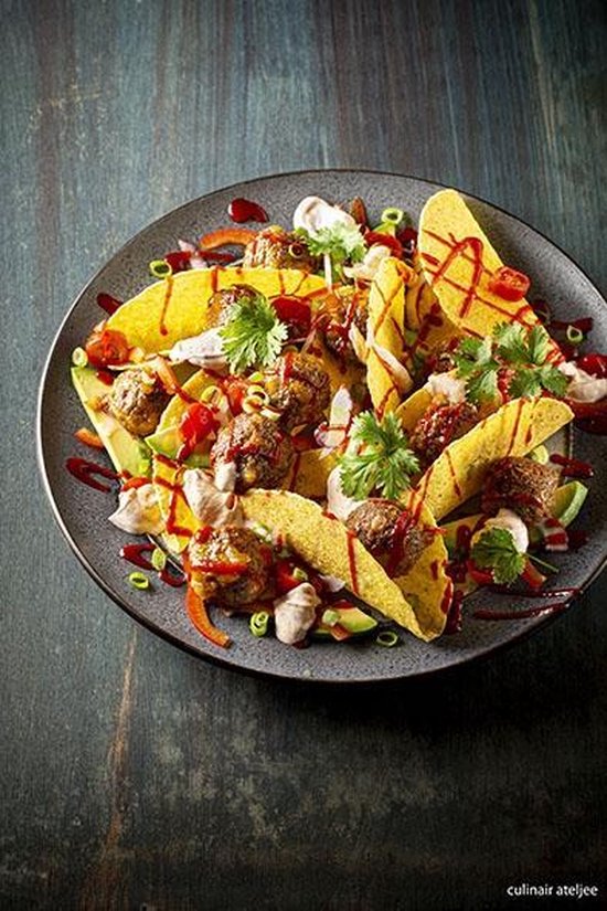 Gevulde taco's met gehaktballen, avocado, tomaat en koriander, besprenkeld met saus op een grijs bord.