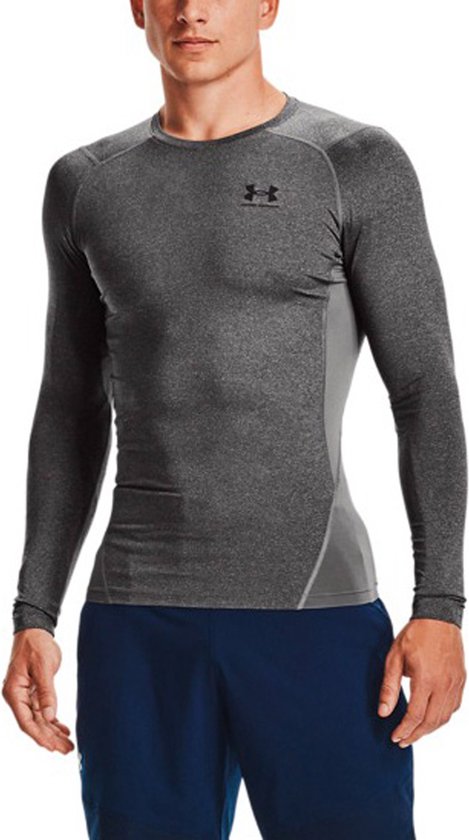 Bovenlichaam van een man in een grijs melange Under Armour sportshirt met lange mouwen en een blauwe sportbroek.