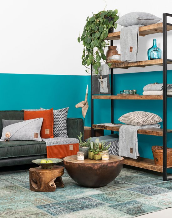 Zitkamerinterieur met een groene bank, diverse gebreide kussens, plaids, planten en een houten salontafel.