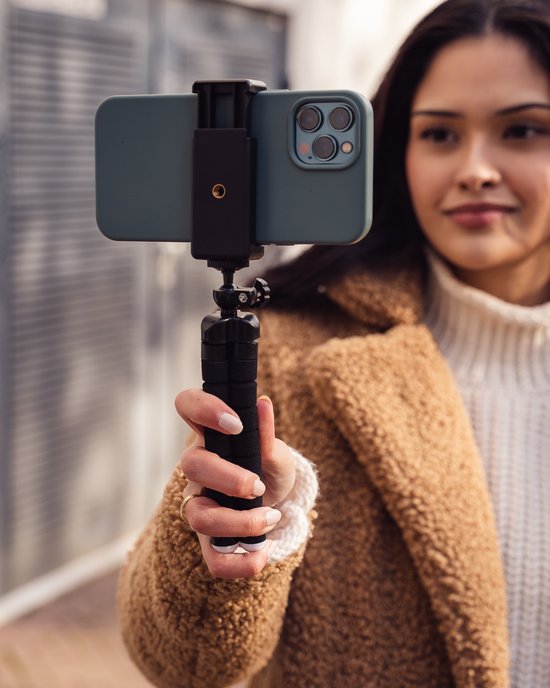 Een vrouw met een bruine teddy jas houdt een smartphone vast op een flexibel statief.