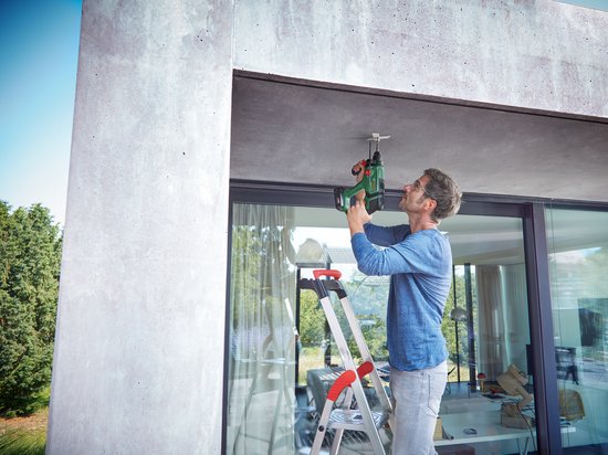 Man op ladder monteert met groene Bosch boorhamer aan plafond.