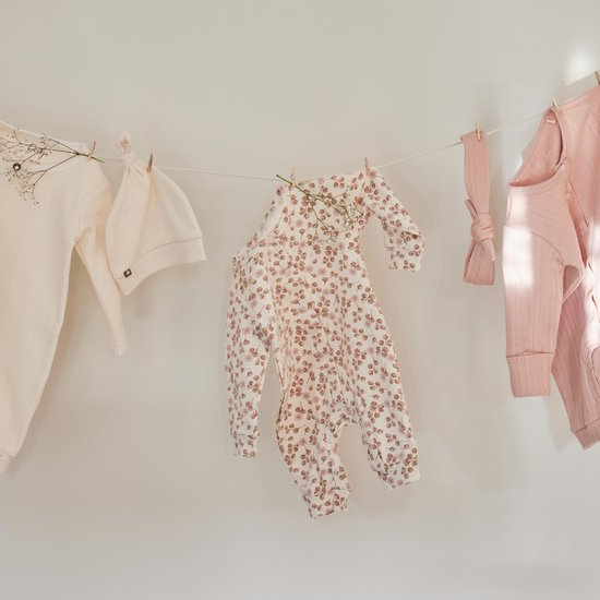 Een gebroken witte romper met muts en roze kledingstukken met bloemenprint, gedroogd aan een waslijn.