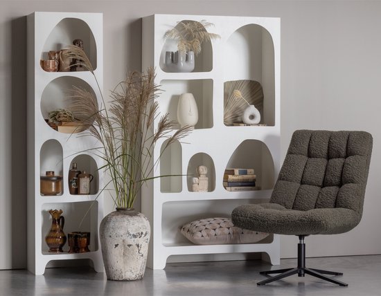 Moderne witte open kast naast een stoere donkergrijze fauteuil. De kast bevat decoraties en een vaas met pampasgras.