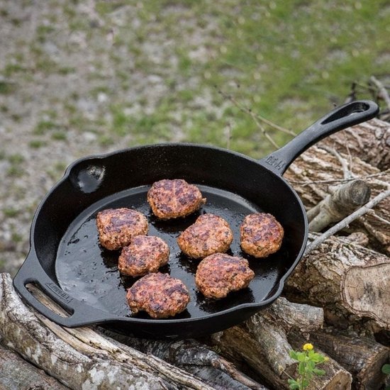 Gietijzeren pan met zeven gehaktballen, buiten op houthakblokken.