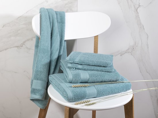 Serviettes bleu clair de différentes tailles sur une chaise blanche. Une serviette est suspendue au dossier.