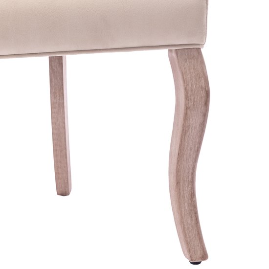 Detail van de gebogen houten poten van een beige fluwelen eetkamerstoel.