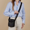 Vrouw in blauw overhemd en witte broek draagt een zwarte leren schoudertas van The Chesterfield Brand.