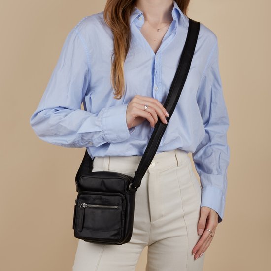 Vrouw in blauw overhemd en witte broek draagt een zwarte leren schoudertas van The Chesterfield Brand.