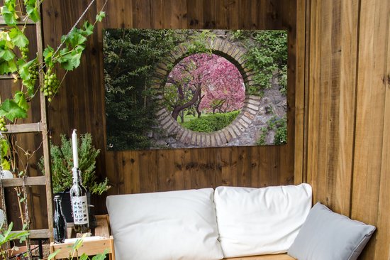 Vue d'un cerisier sakura en fleurs à travers un cercle de pierre. Accroché à un mur en bois avec un banc.