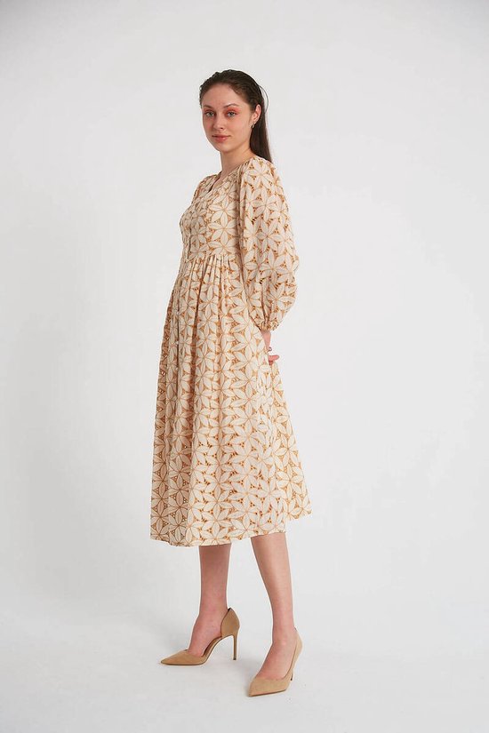 Model in crèmekleurige jurk met pofmouwen en camel geometrisch patroon, op hoge hakken.