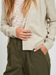 Close-up van een beige gebreid vest met bloemenprint top en olijfgroene broek.