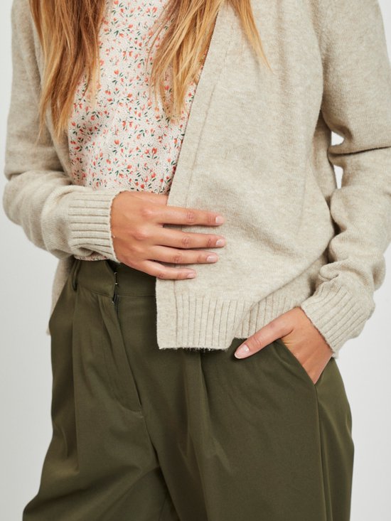 Close-up van een beige gebreid vest met bloemenprint top en olijfgroene broek.