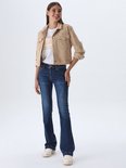 Model in een beige spijkerjack, wit T-shirt en donkerblauwe flared jeans met witte sneakers.