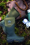 Groene Muck Boot Muckmaster laarzen liggen op mos bij een weekendtas en mokken.